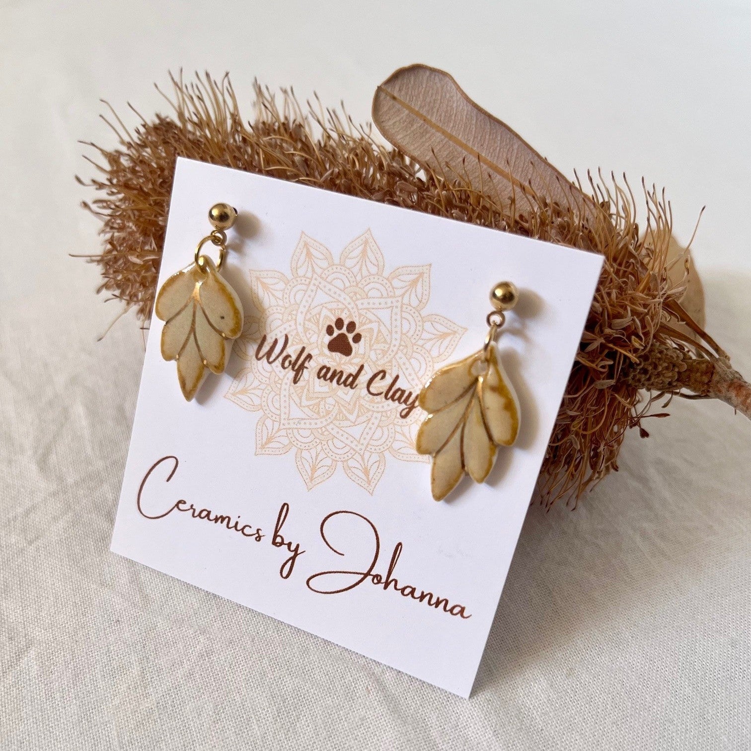 Gold leaf earrings on a 'Wolf and Clay' branded card with decorative elements.