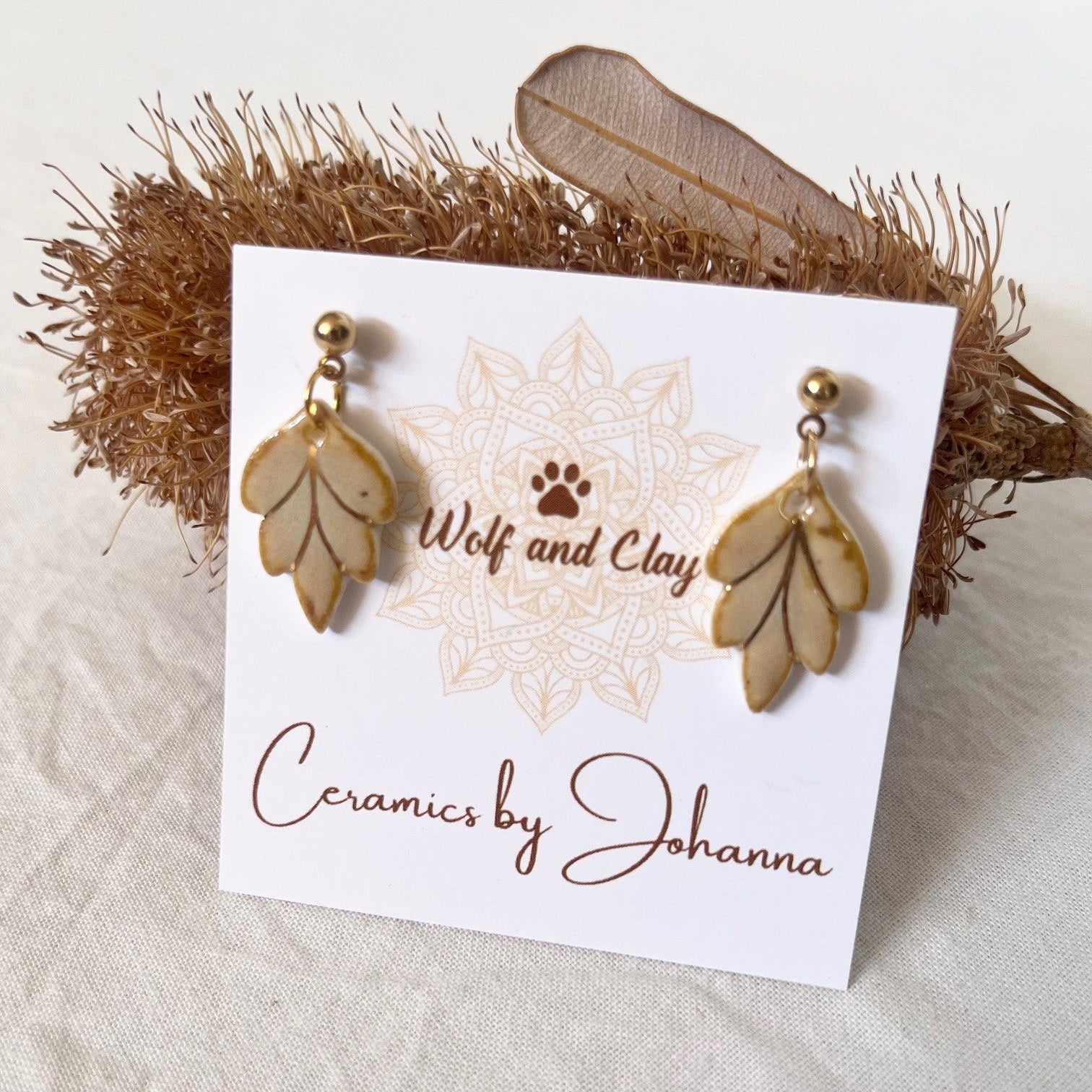 Ceramic leaf-shaped earrings on a 'Wolf and Clay' branded card with a decorative background.