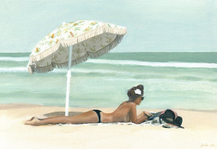 Woman sunbathing under a large beach umbrella on a sandy beach with ocean in the background