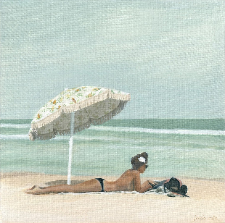 Woman lying on a beach under a large umbrella with a light blue ocean and sky in the background.