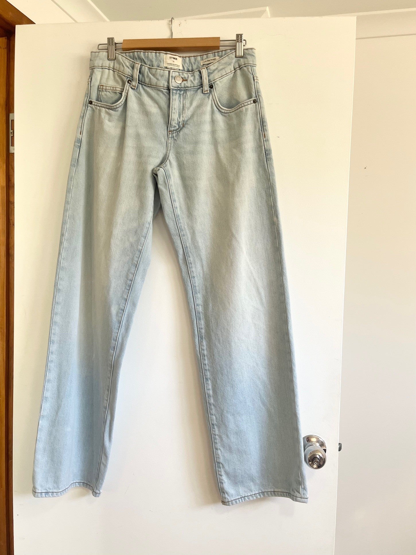 Light blue jeans hanging on a wooden hanger against a white wall.