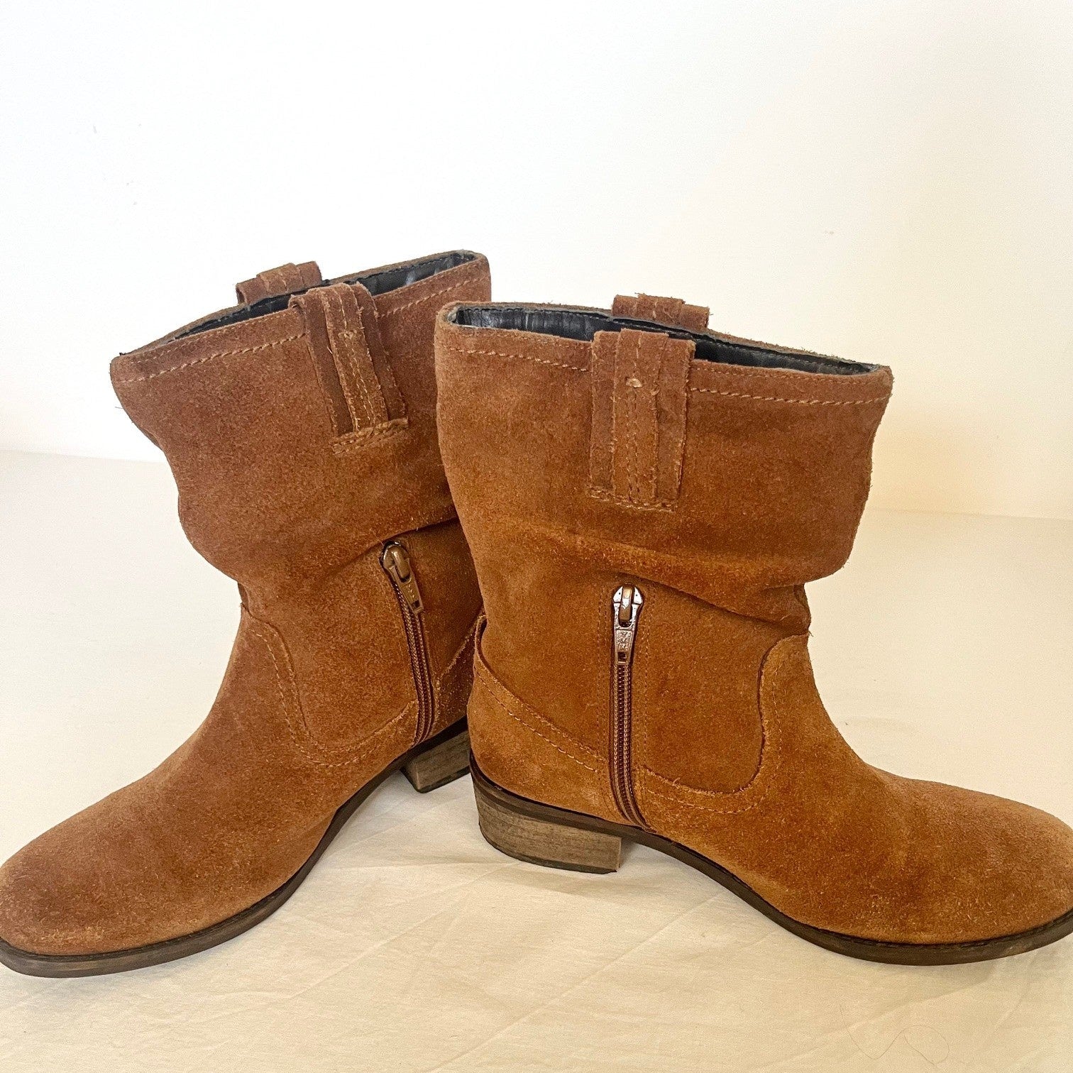 Pair of brown suede boots with zippers on a beige surface