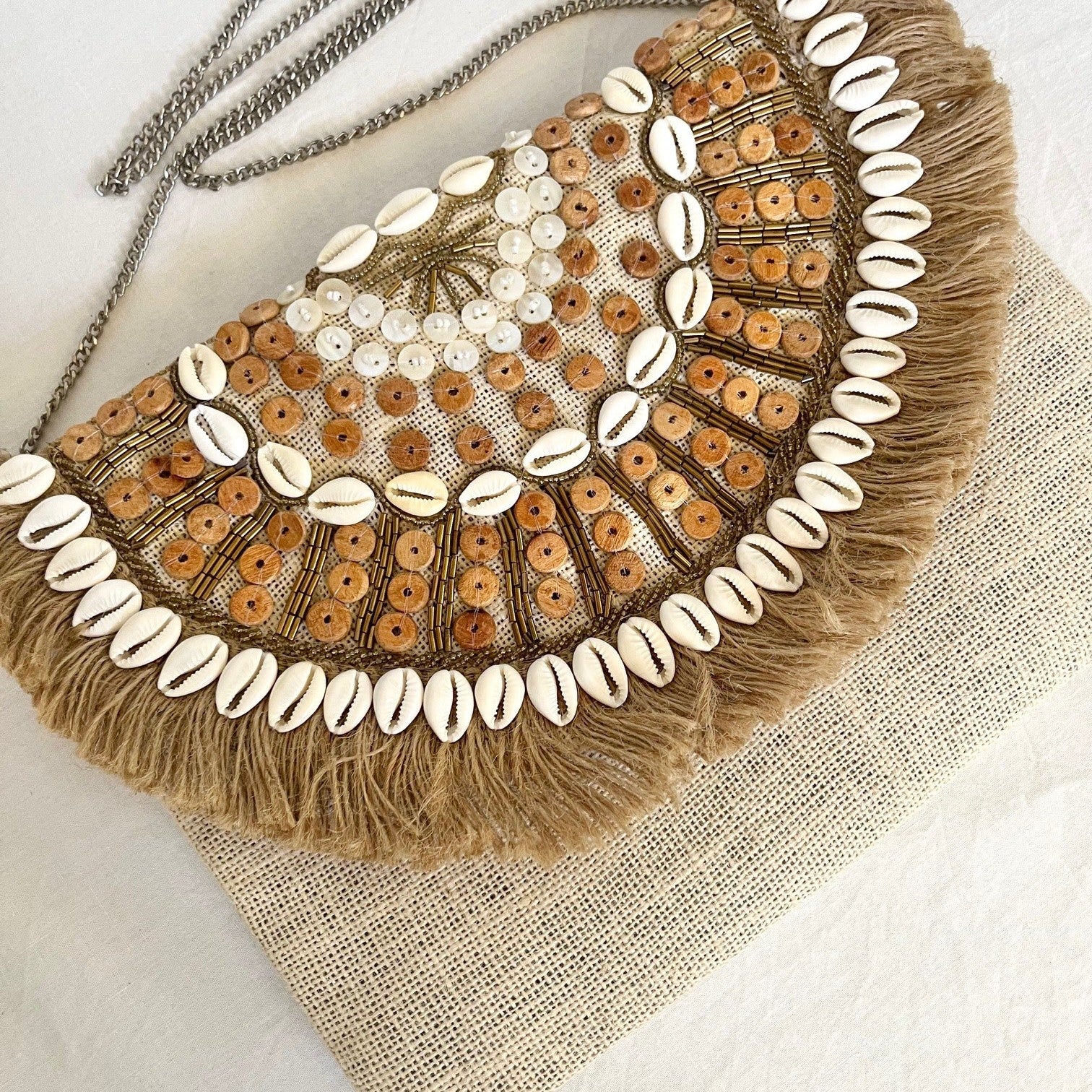 Decorative clutch bag with shell embellishments and tassels on a textured surface