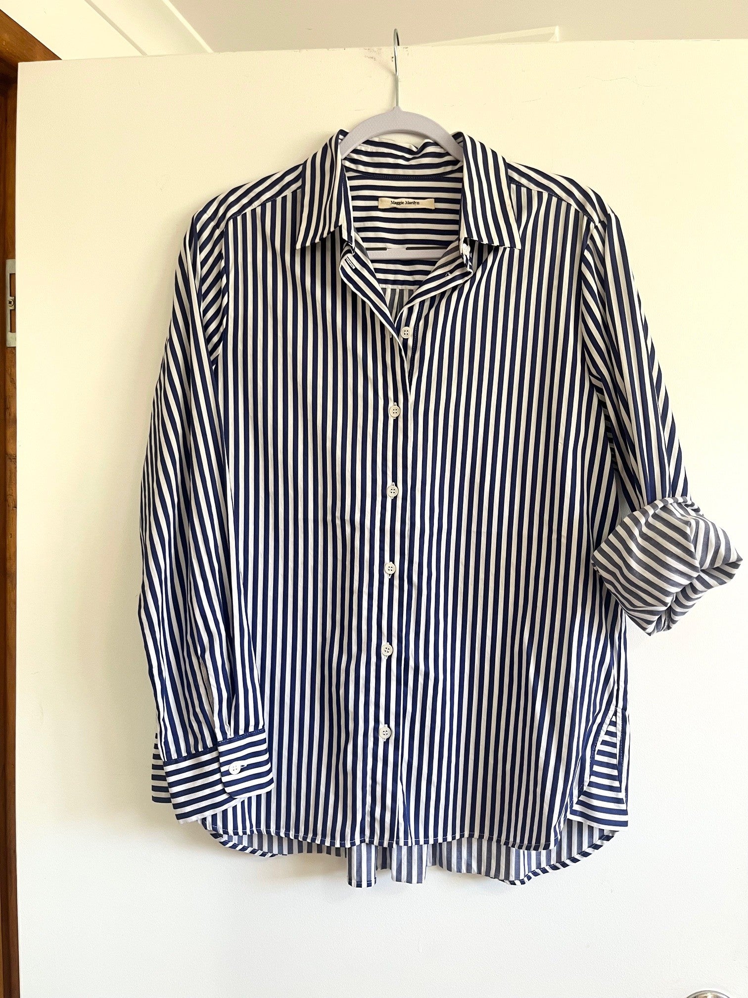Navy and white striped shirt on a hanger against a white wall.