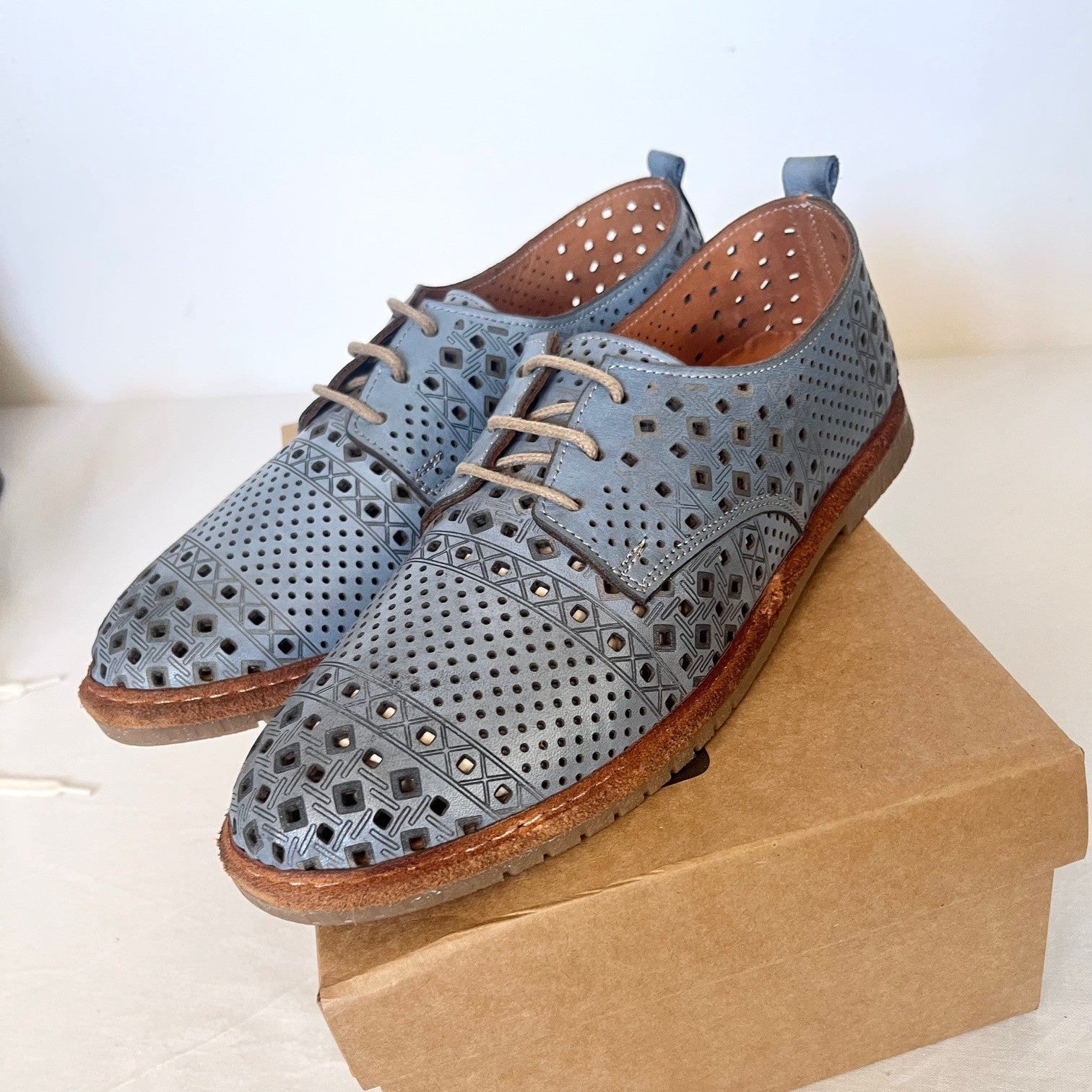 Pair of blue perforated shoes on a cardboard box with a white background