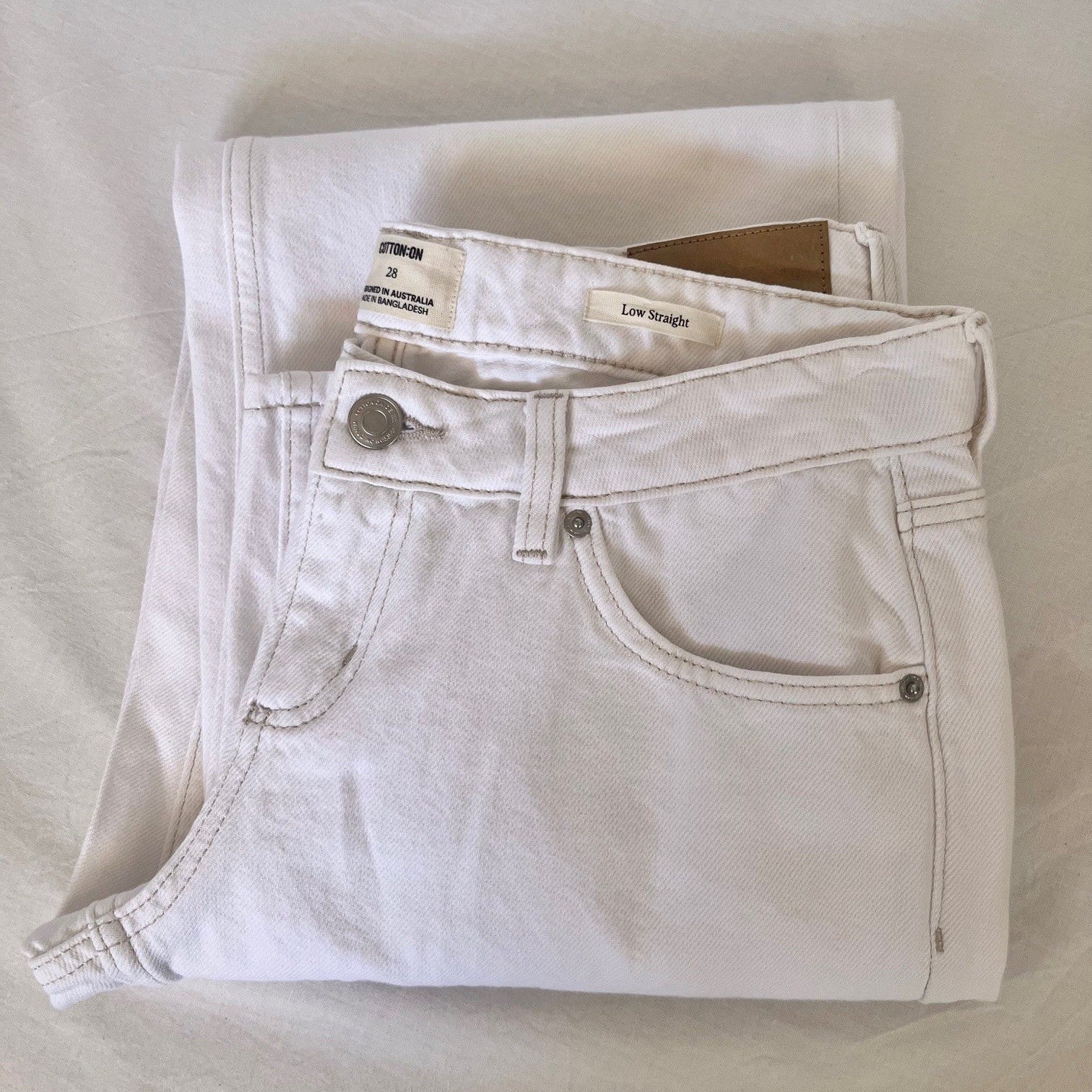 Folded white jeans with brown stitching on a light gray background