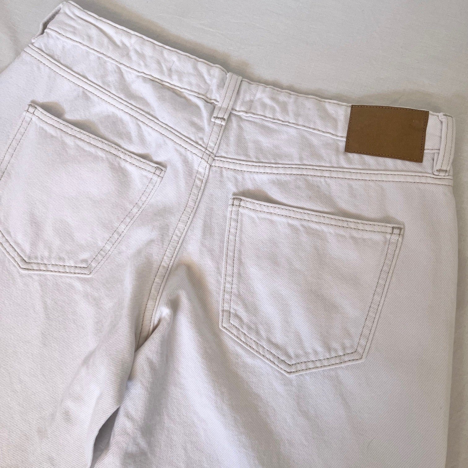 White denim jeans with a brown label on a light gray background