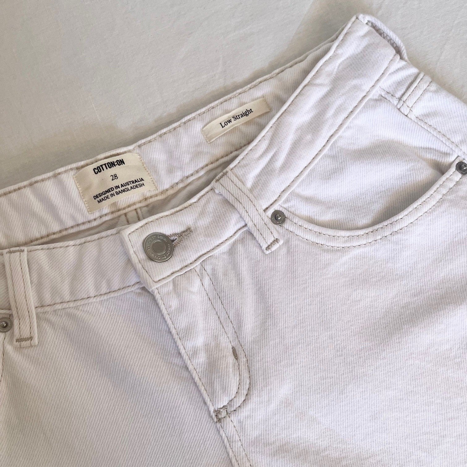 Close-up of white jeans with a visible Cotton On label on a light background