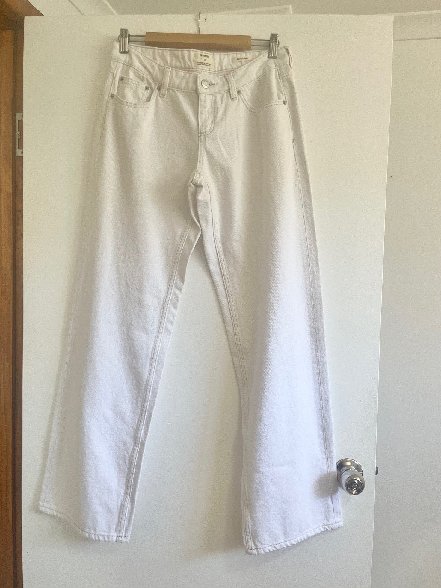 White jeans hanging on a door handle against a white wall